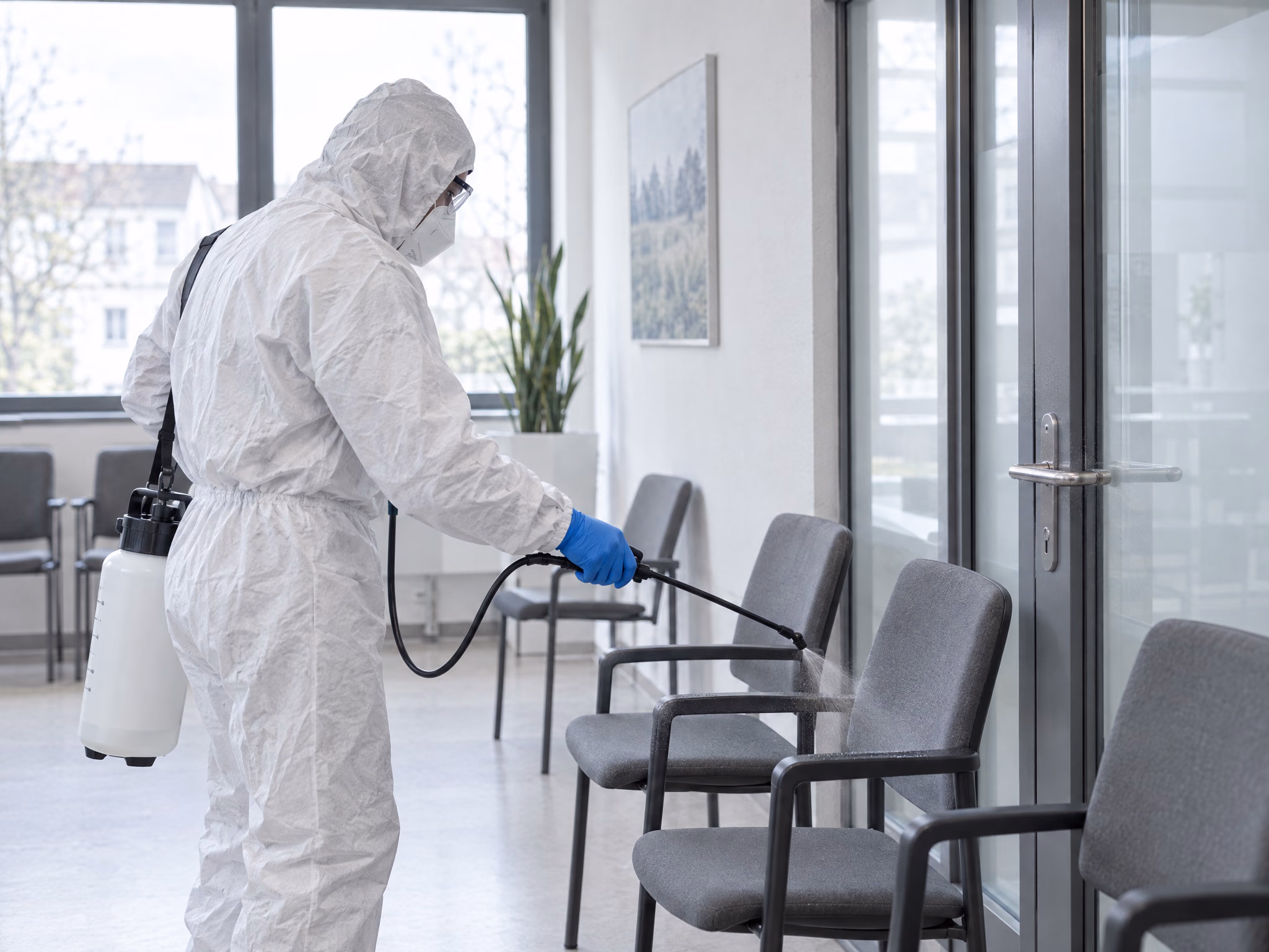 Desinfektion eines Praxis-Wartezimmers in Schutzanzug und Maske